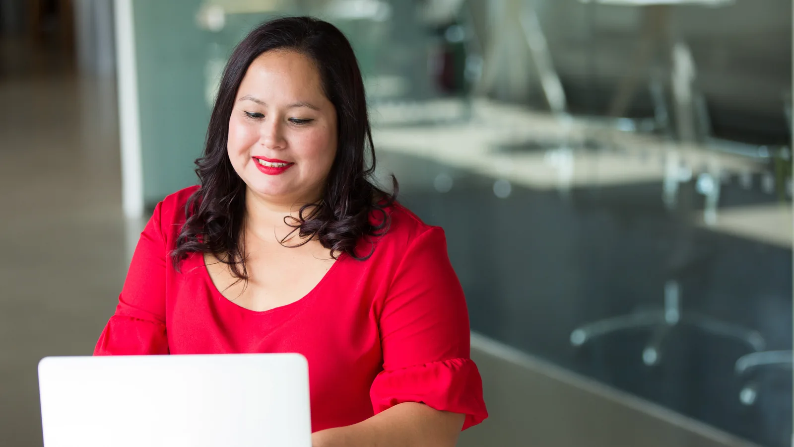 A professional at a laptop in a glass-walled office