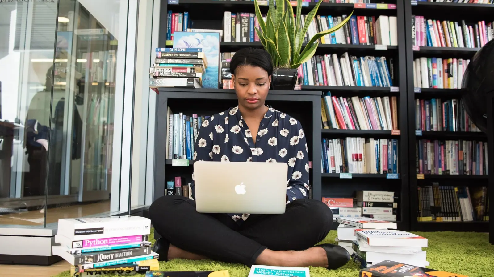 A woman working at a laptop among bookshelves
