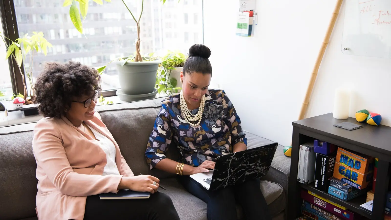 Two women working on laptops on a sofa