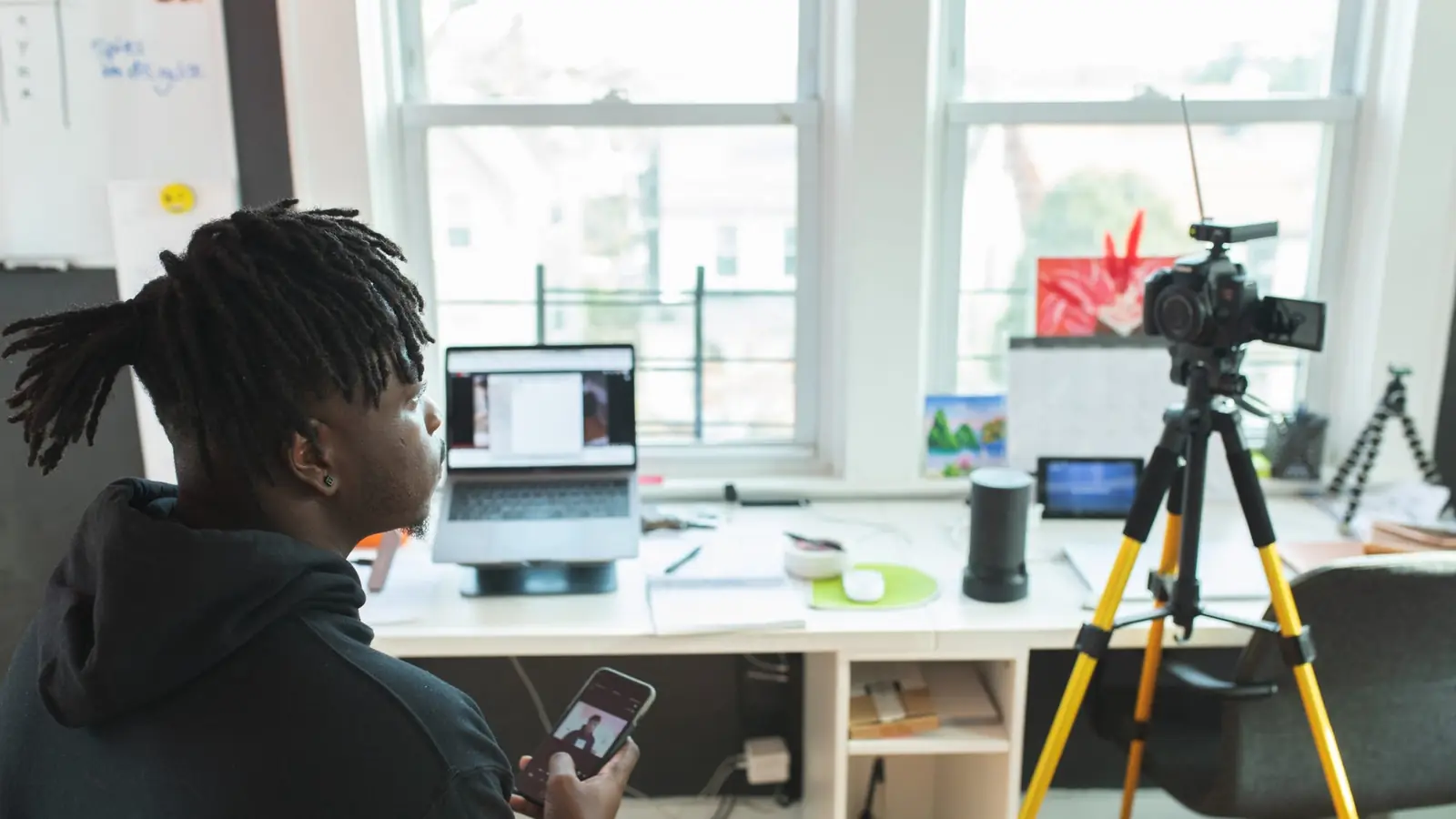 A host at a desk with a laptop and a camera on a tripod, set up to run a live session