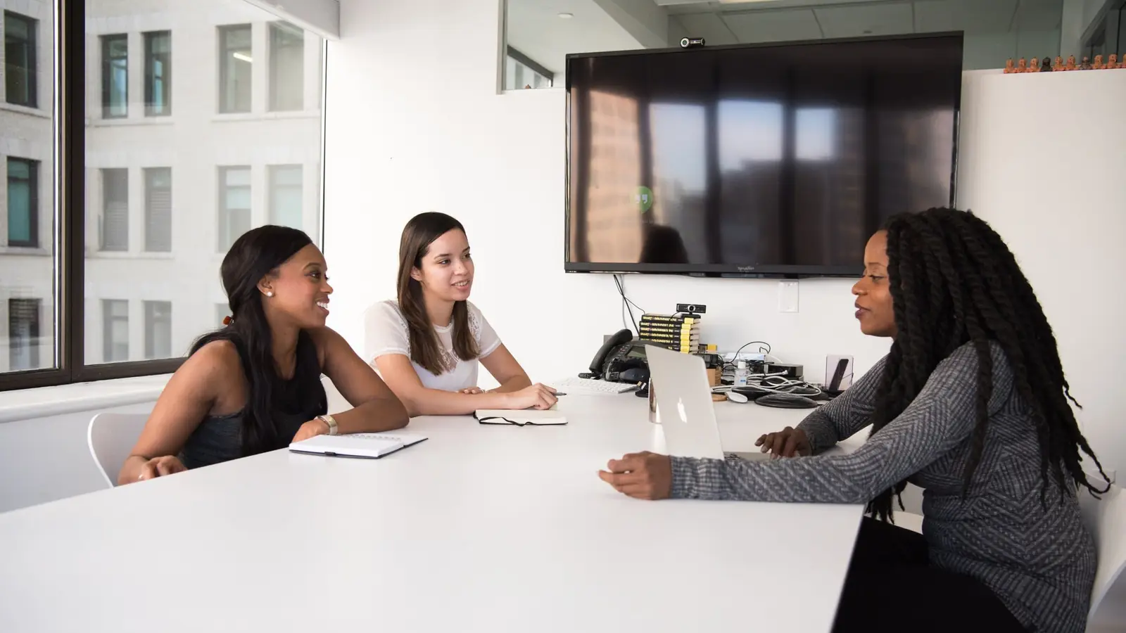 Three women seated around a white meeting table