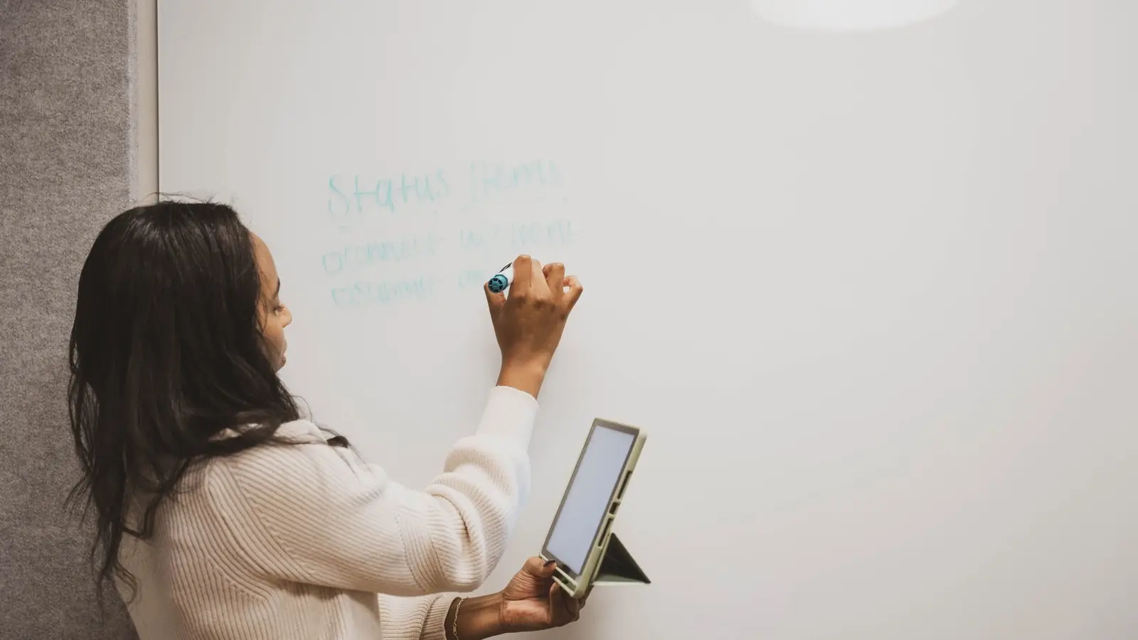A woman writing on a whiteboard while holding a tablet