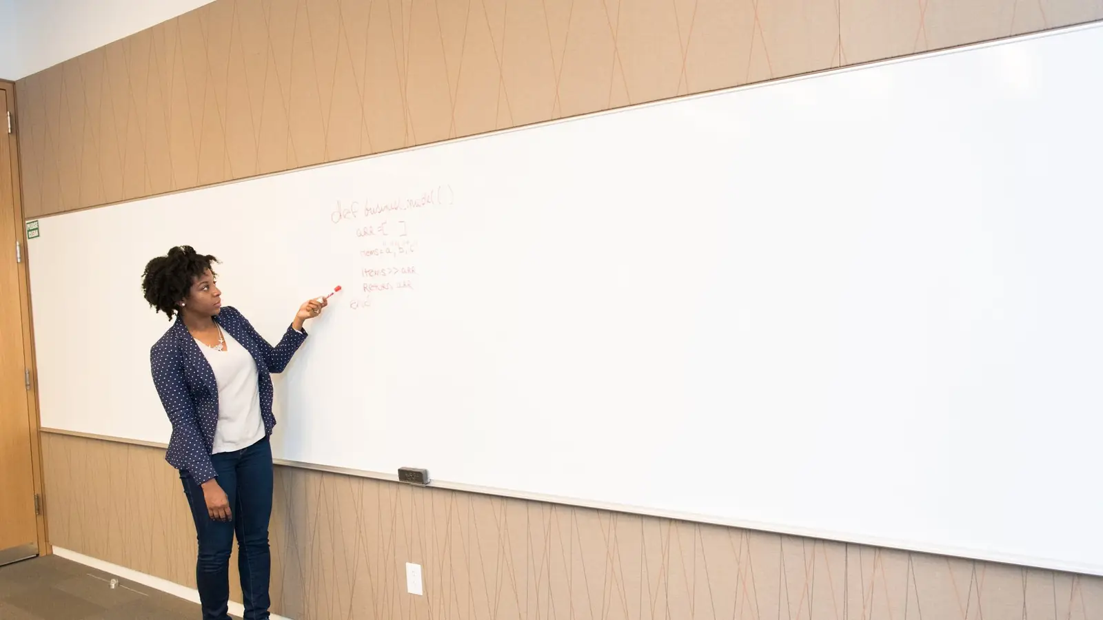 A woman writing on a wall-mounted whiteboard
