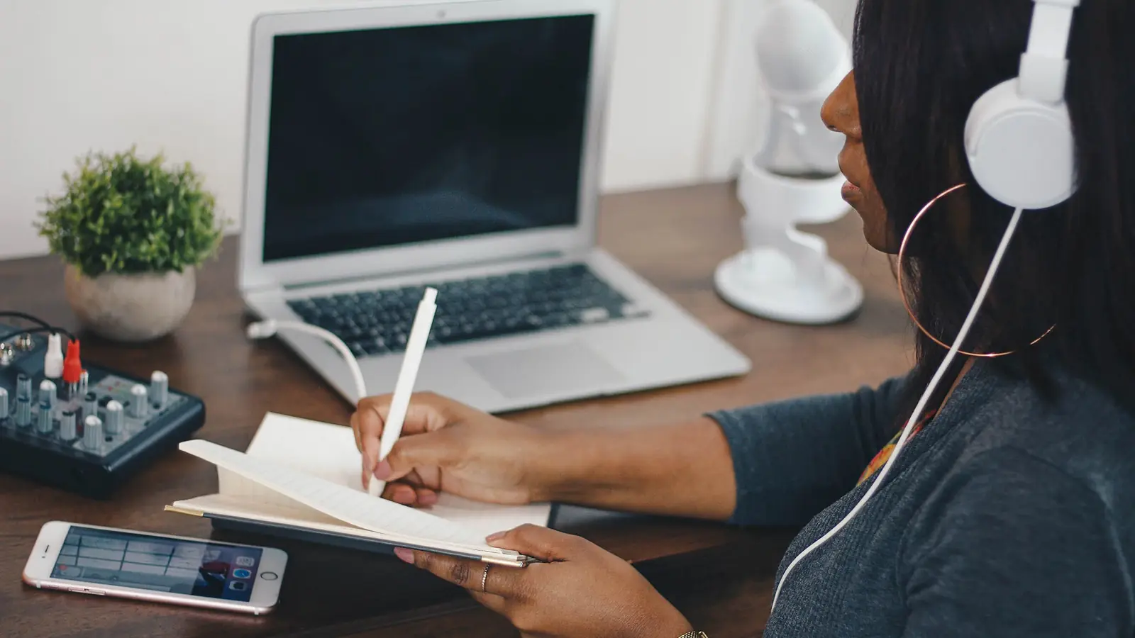 A woman writing notes while wearing headphones